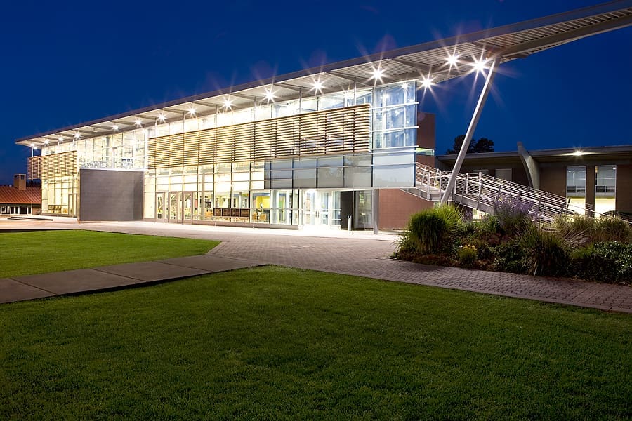 Modern building with large glass windows and a metal overhang, illuminated at night, with a lawn and landscaped area in the foreground—showcasing Kinney’s commitment to Building Better Together for a Greener Tomorrow.